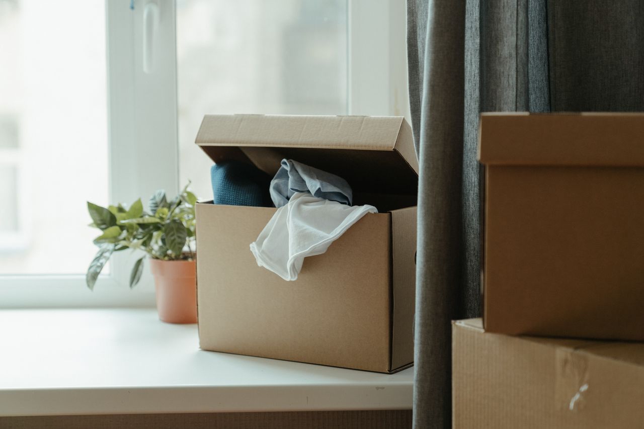 about-02 Open cardboard box with clothes by window, symbolizing moving or relocation.